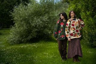 Two people wearing patterned cardigans standing in a grassy area with trees.