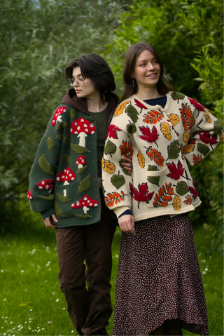 Two people wearing patterned cardigans standing outdoors with greenery in the background